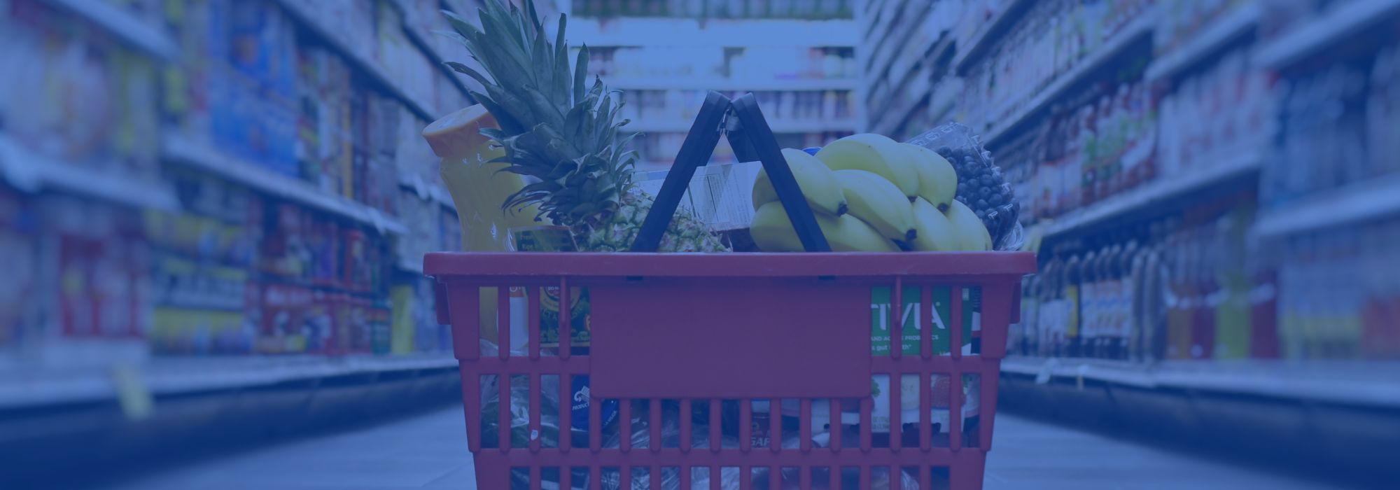 basket full of groceries in center of image; grocery store aisles behind