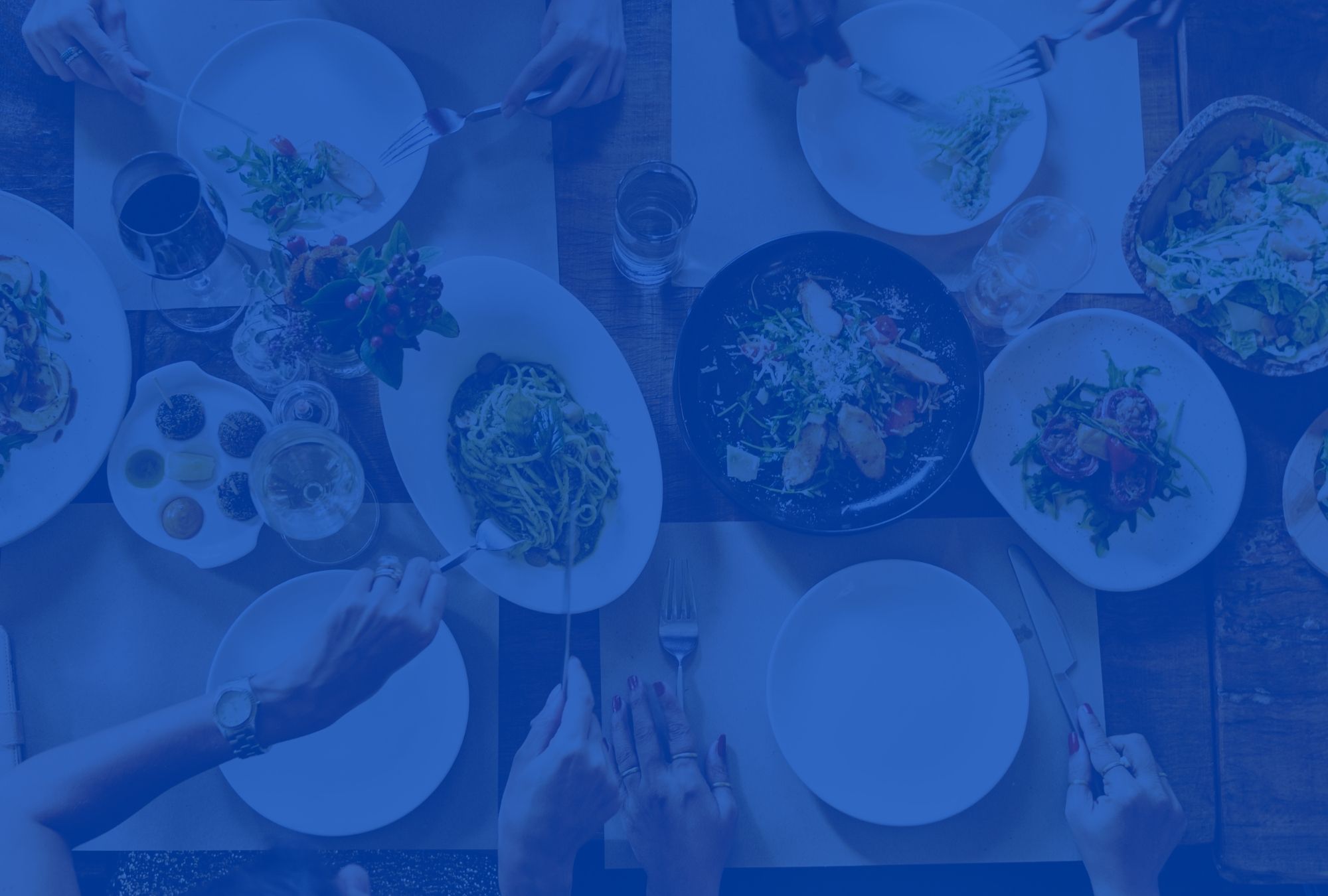 Different plates of food on table, hands reaching across to grab various dishes.