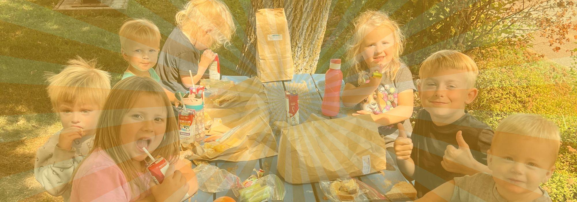 Children eat lunch at picnic table behind a yellow sunburst