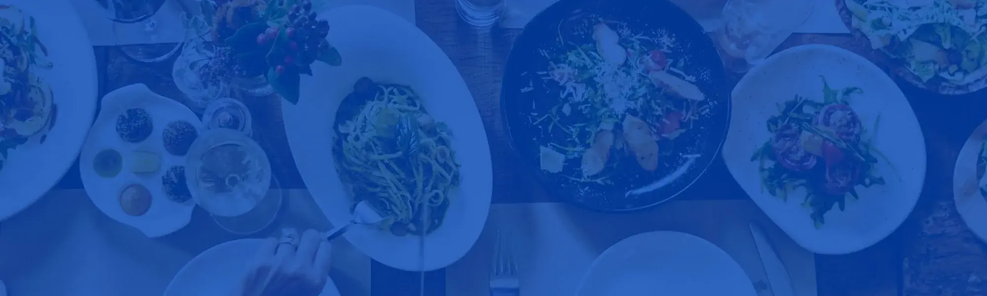 Different plates of food on table, hands reaching across to grab various dishes.