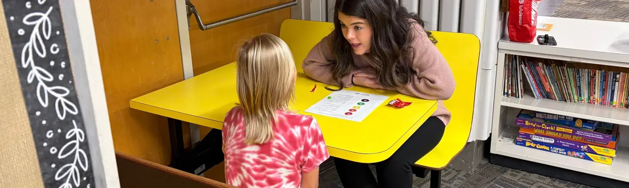 Lunch Buddies mentor and mentee play a game at a yellow table.