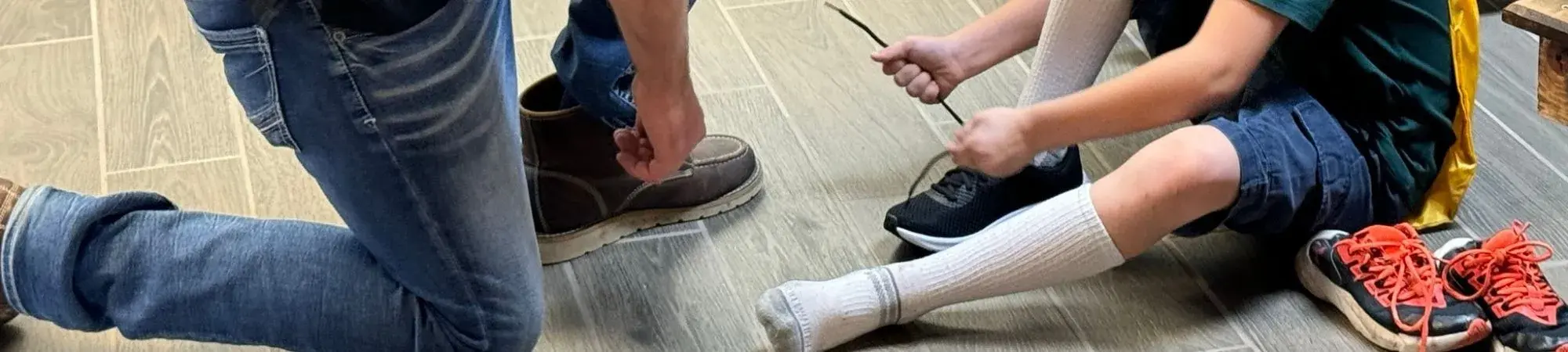 Student tries on new school shoes with the help of a Step Into School volunteer