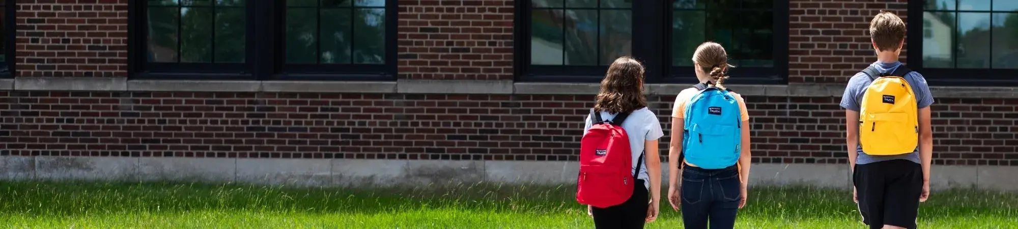 Students walk toward school wearing backpacks