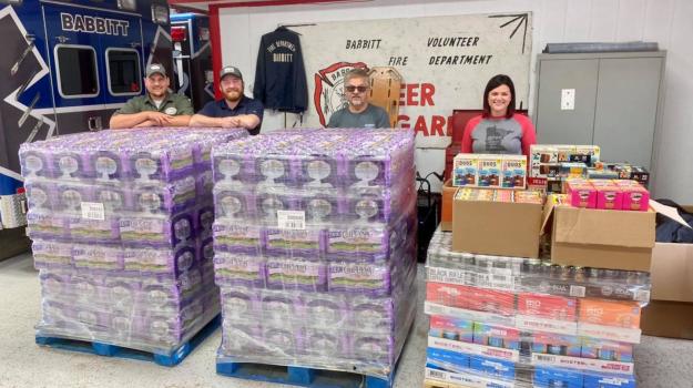 D & D employees (left) rest elbows on wo pallets of water bottles next to Babbitt Fire Department staff in middle and United Way of Northeastern Minnesota Executive Director Erin Shay at right who is behind a pallet of sports drinks, energy drinks, and snacks at the Babbitt Fire Station