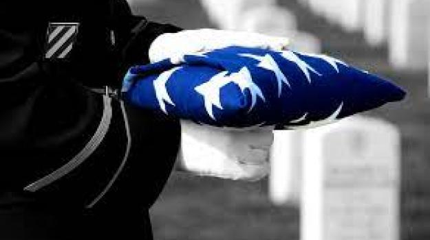 Black and white photo of a soldier carrying an American flag; flag is in blue