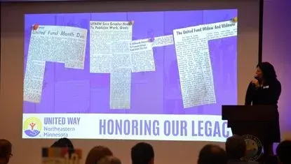 UWNEMN Executive Director Erin Shay reads newspaper clippings from 1966 at UWNEMN's 60th Annual Celebration, presented by Fairview